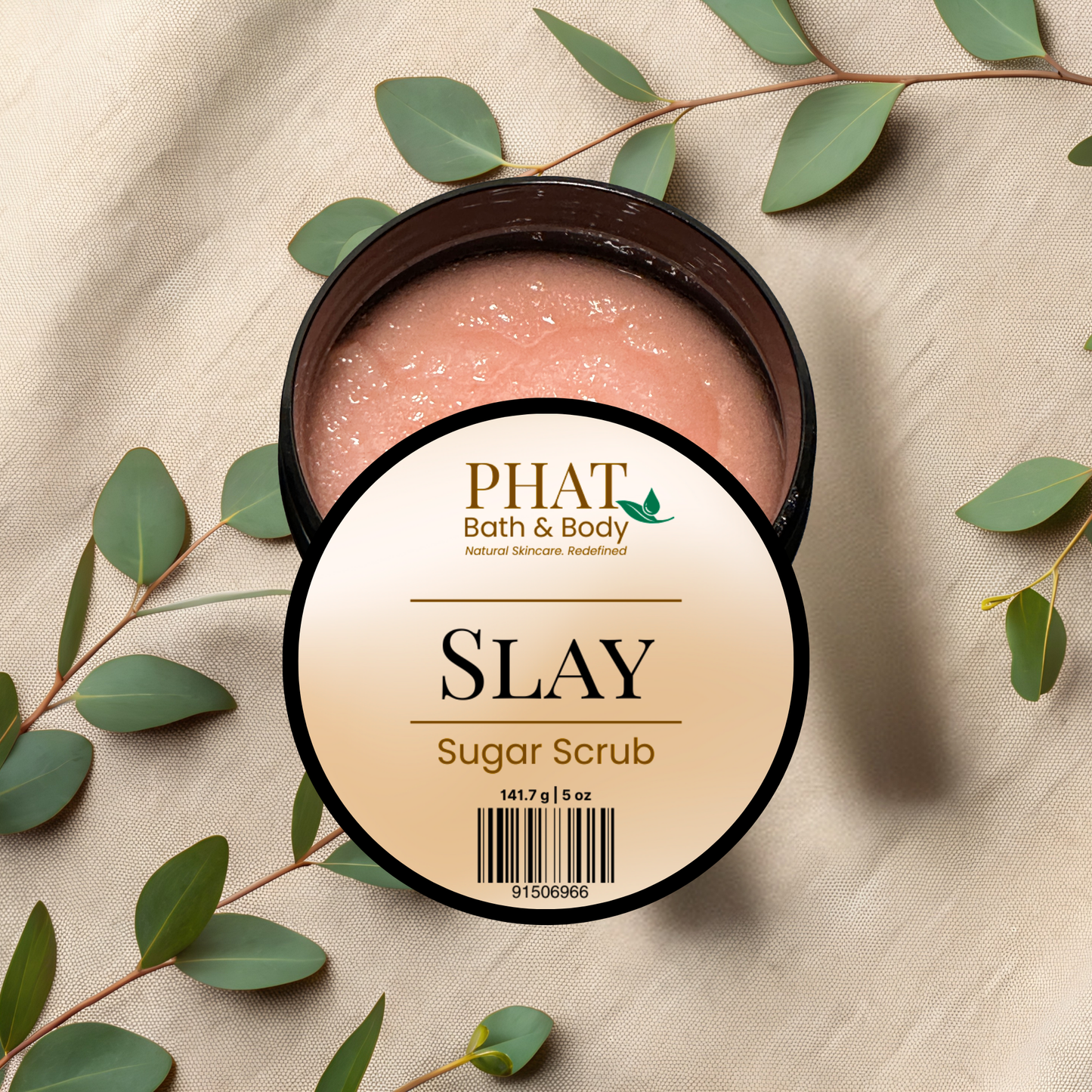 Slay sugar scrub from Phat Bath & Body on a beige fabric background with green leaves.