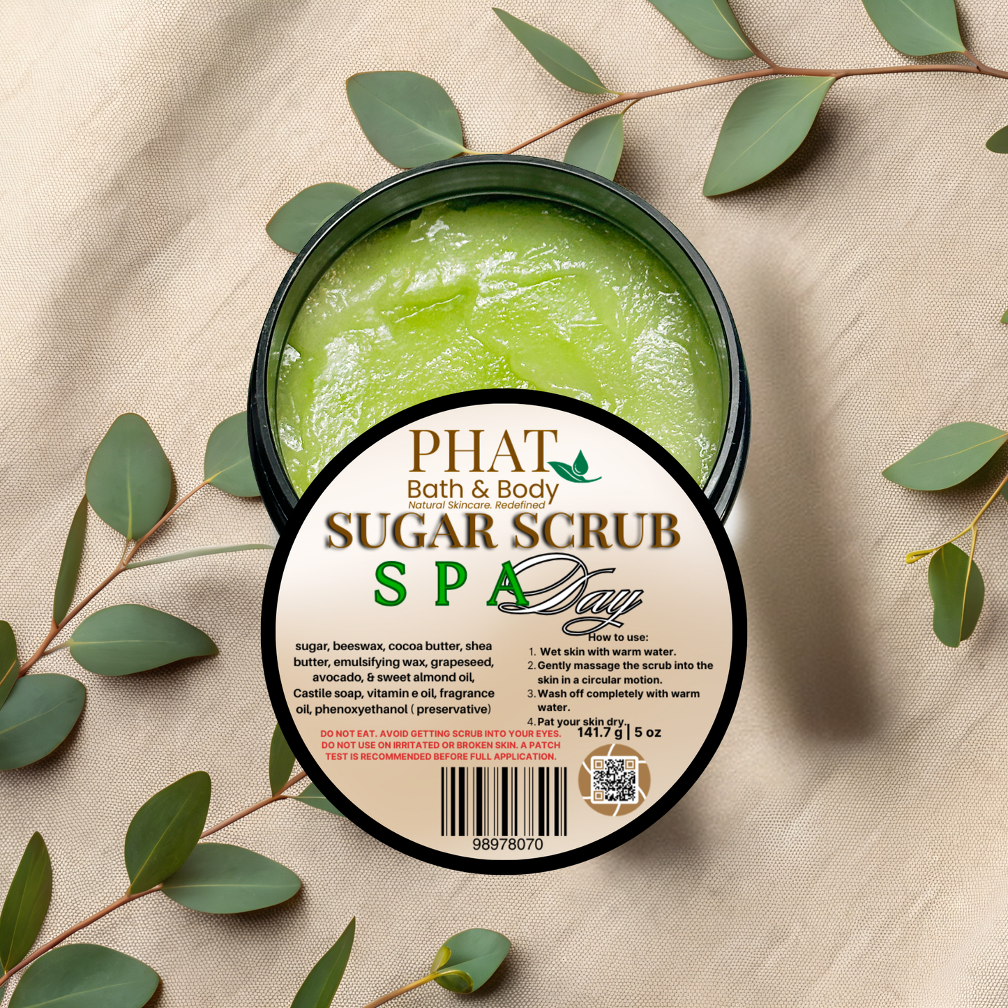 Green sugar scrub in a container with a label on a beige fabric background with green leaves.