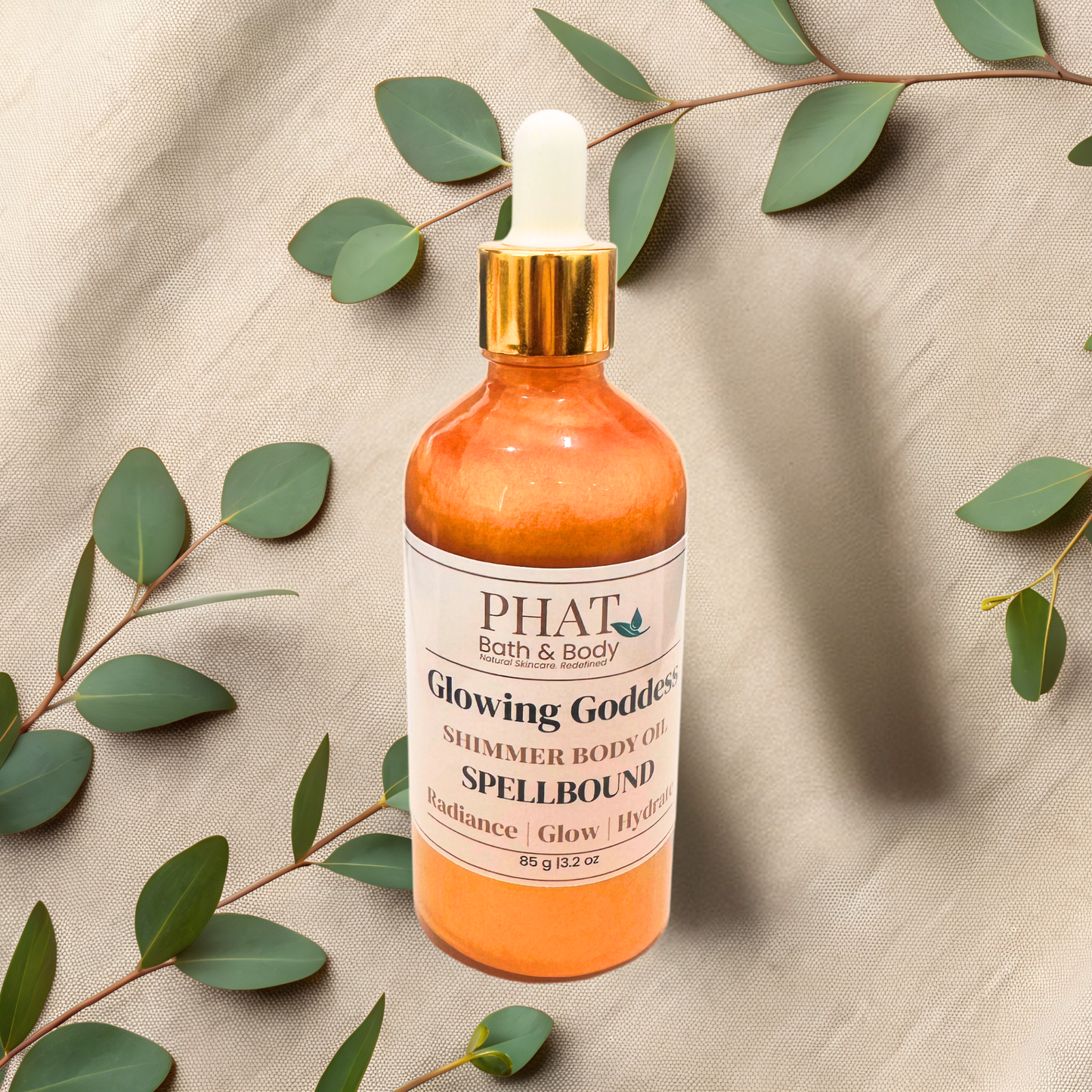 Bottle of PHAT Bath & Body shimmer oil with green leaves on a textured beige background