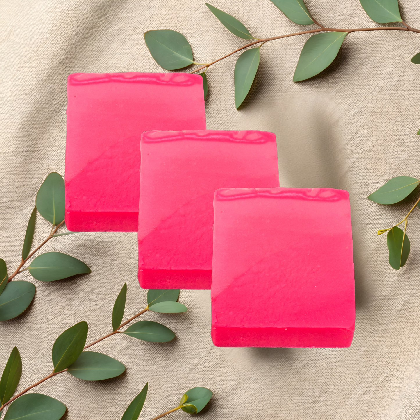 Three pink soap bars on a beige fabric background with green leaves.