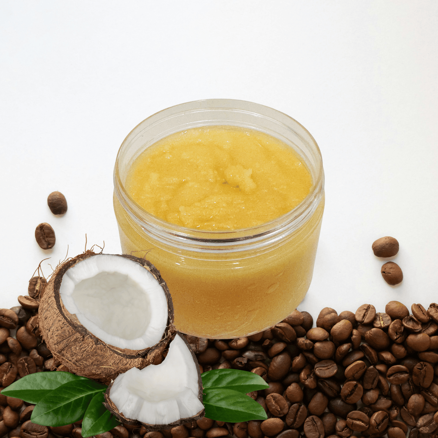 Jar of sugar scrub surrounded by coconut halves and coffee beans on a white background