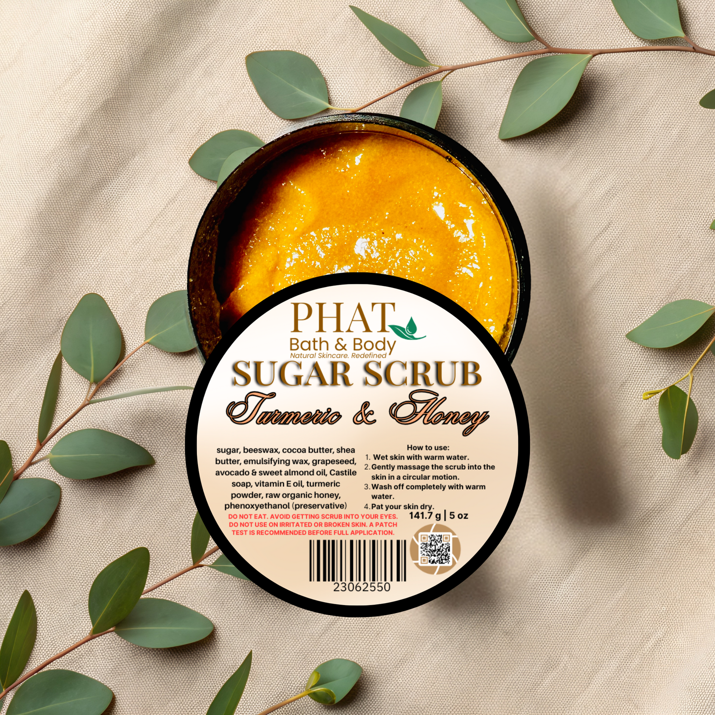 Open container of Phat Bath & Body sugar scrub with leaves on a beige fabric background