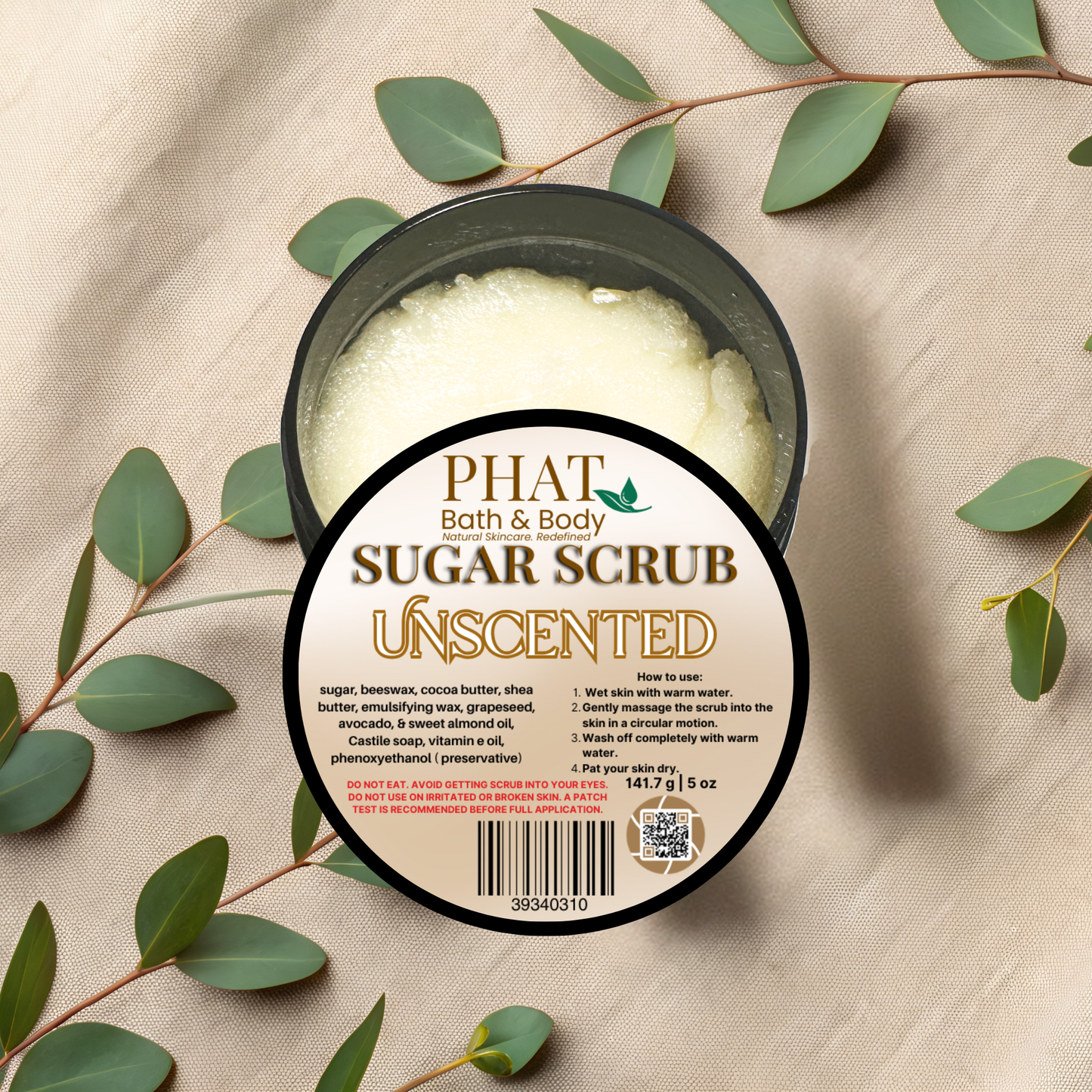 Jar of Phat Bath & Body sugar scrub with eucalyptus leaves on a beige fabric background