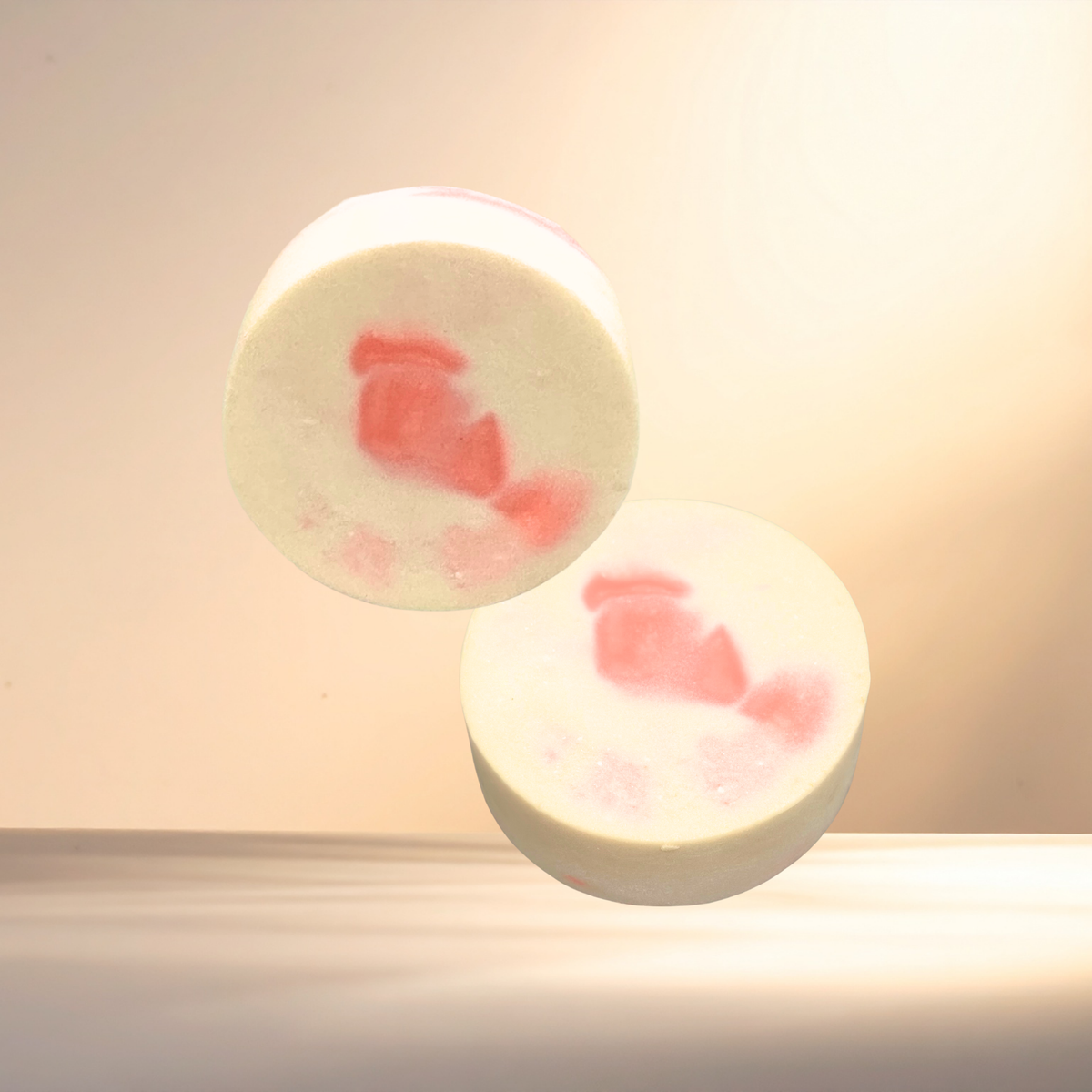 Two round, white soaps with red floral patterns on a light background