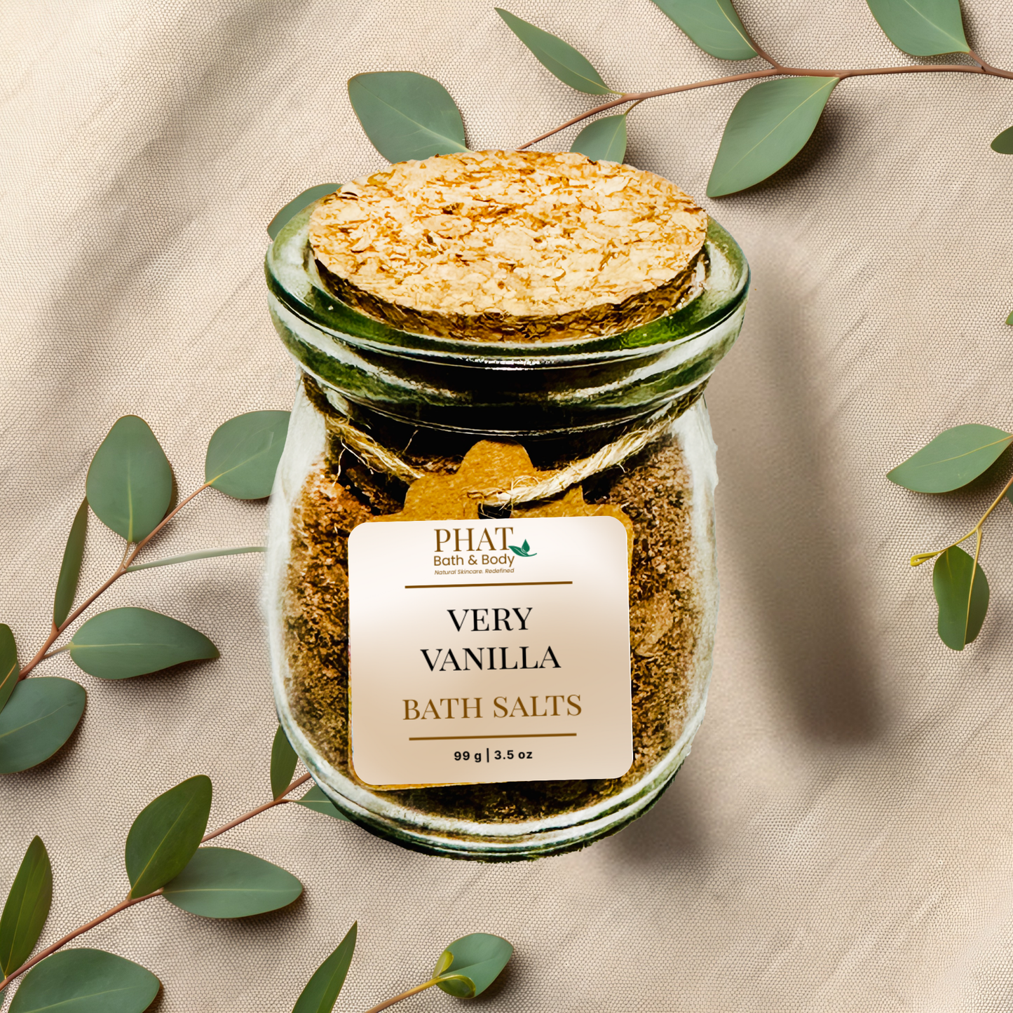 Jar of very vanilla bath salts with a cork lid on a beige fabric background with eucalyptus leaves.