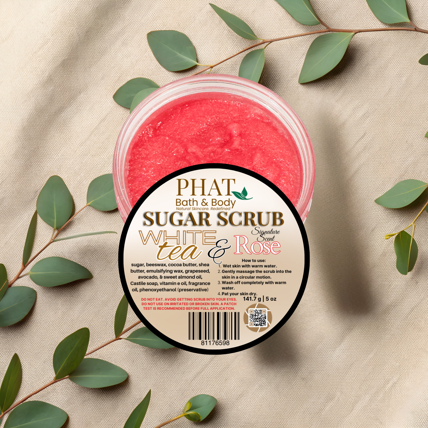 Jar of Phat Bath & Body sugar scrub with green leaves on a beige fabric background