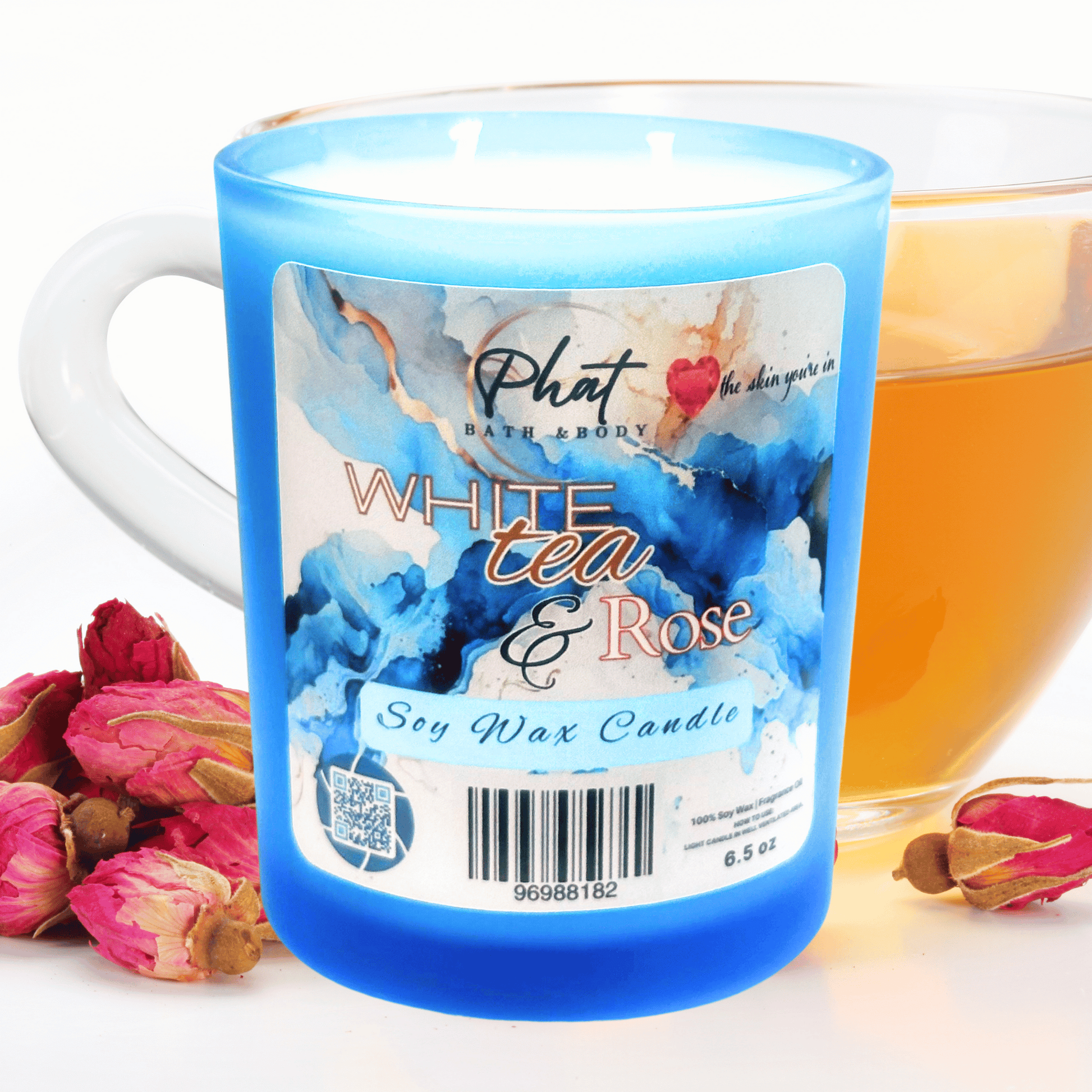 Blue candle labeled 'White Tea & Rose' by Phat Bath & Body with a cup of tea and flowers in the background.