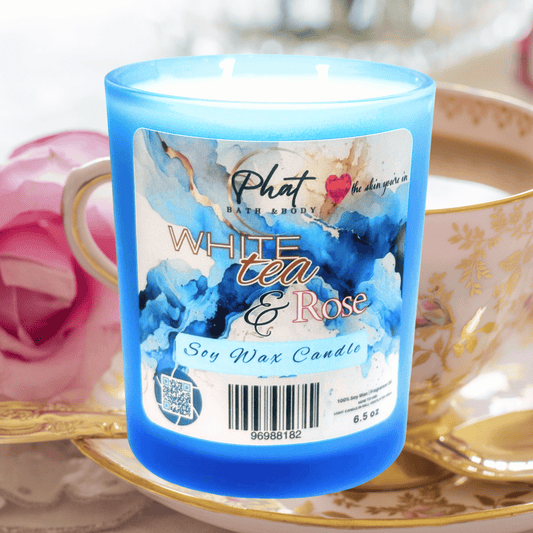 Blue candle labeled 'White Tea & Rose' by Phat Bath & Body on a decorative plate with a tea cup and rose.