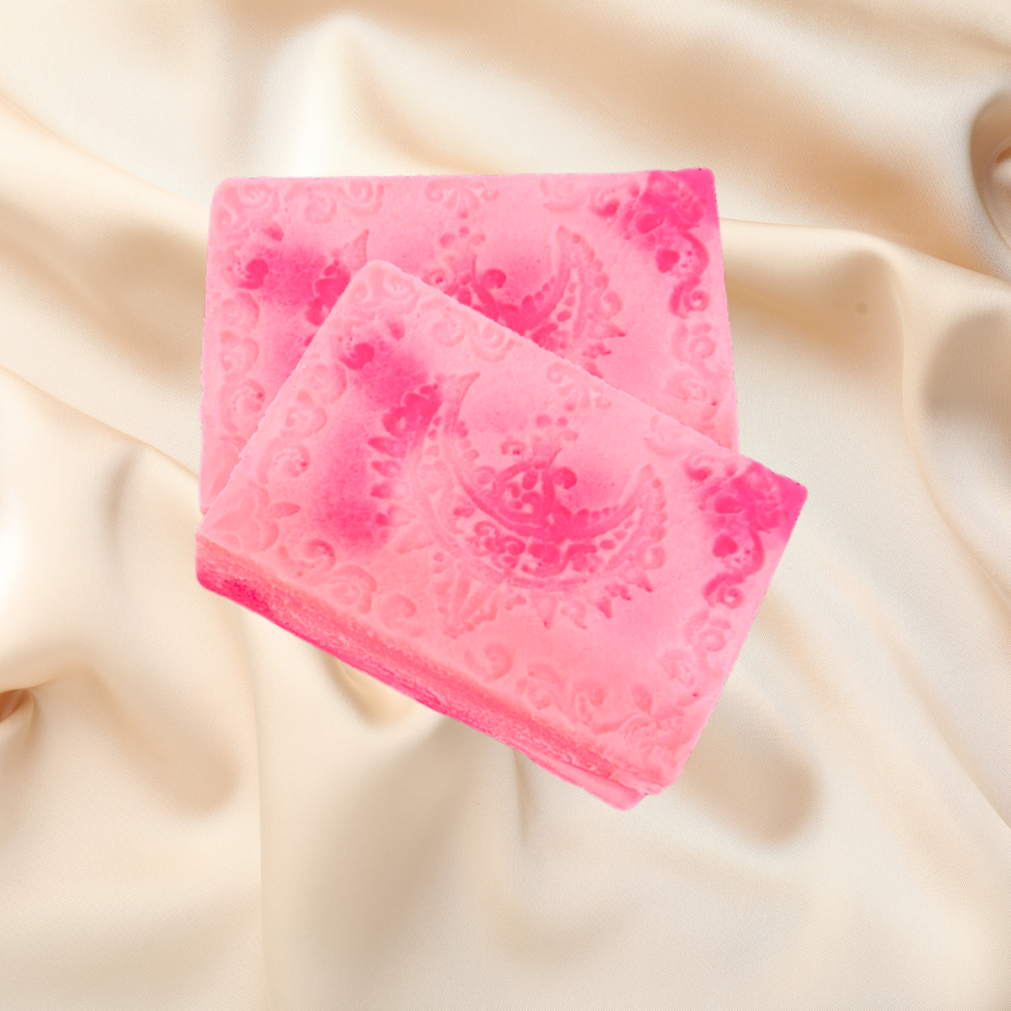Two pink textured soap bars on a beige fabric background