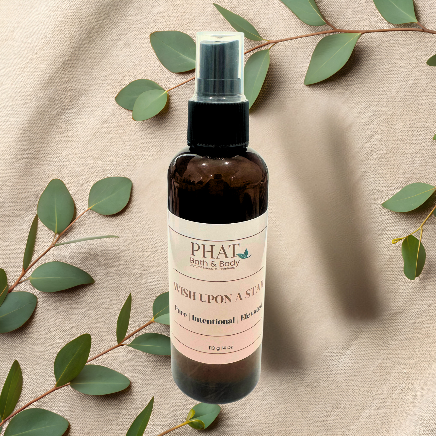 Bottle of 'Wish Upon a Star' by PHAT Bath & Body on a beige fabric background with green leaves.
