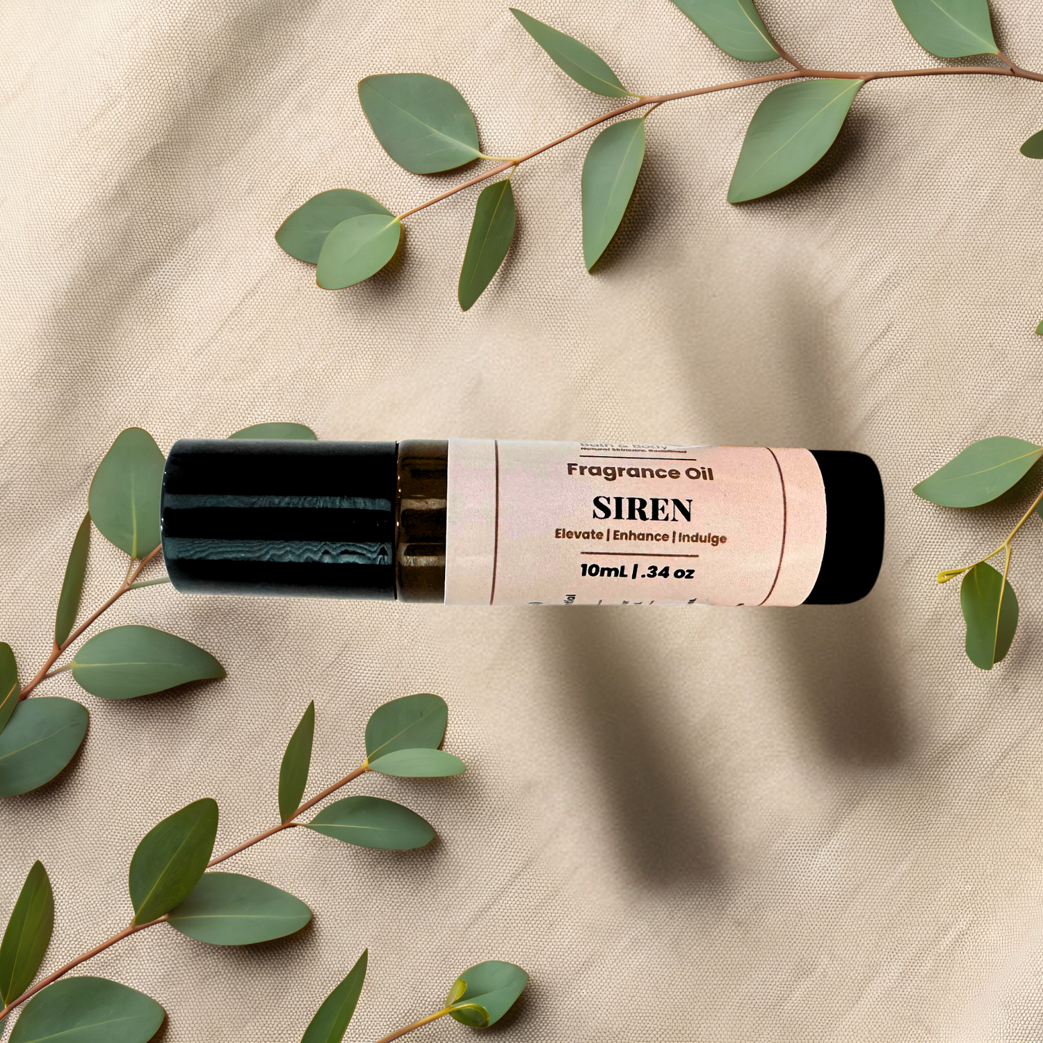 A 10ml bottle of Siren Fragrance Oil, featuring a black cap, displayed horizontally on a beige fabric background decorated with green eucalyptus leaves.