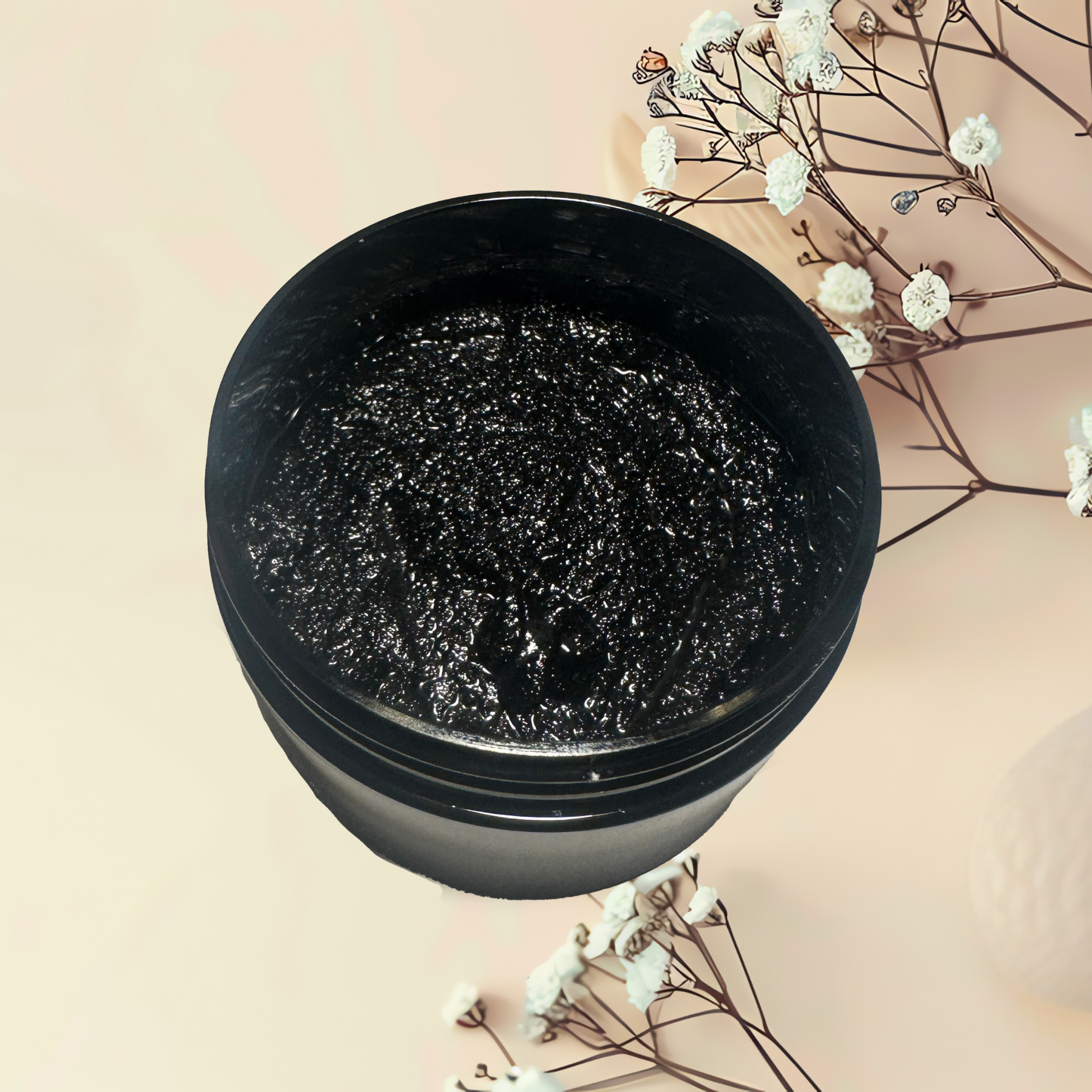 Black jar of cosmetic scrub with decorative flowers on a beige background
