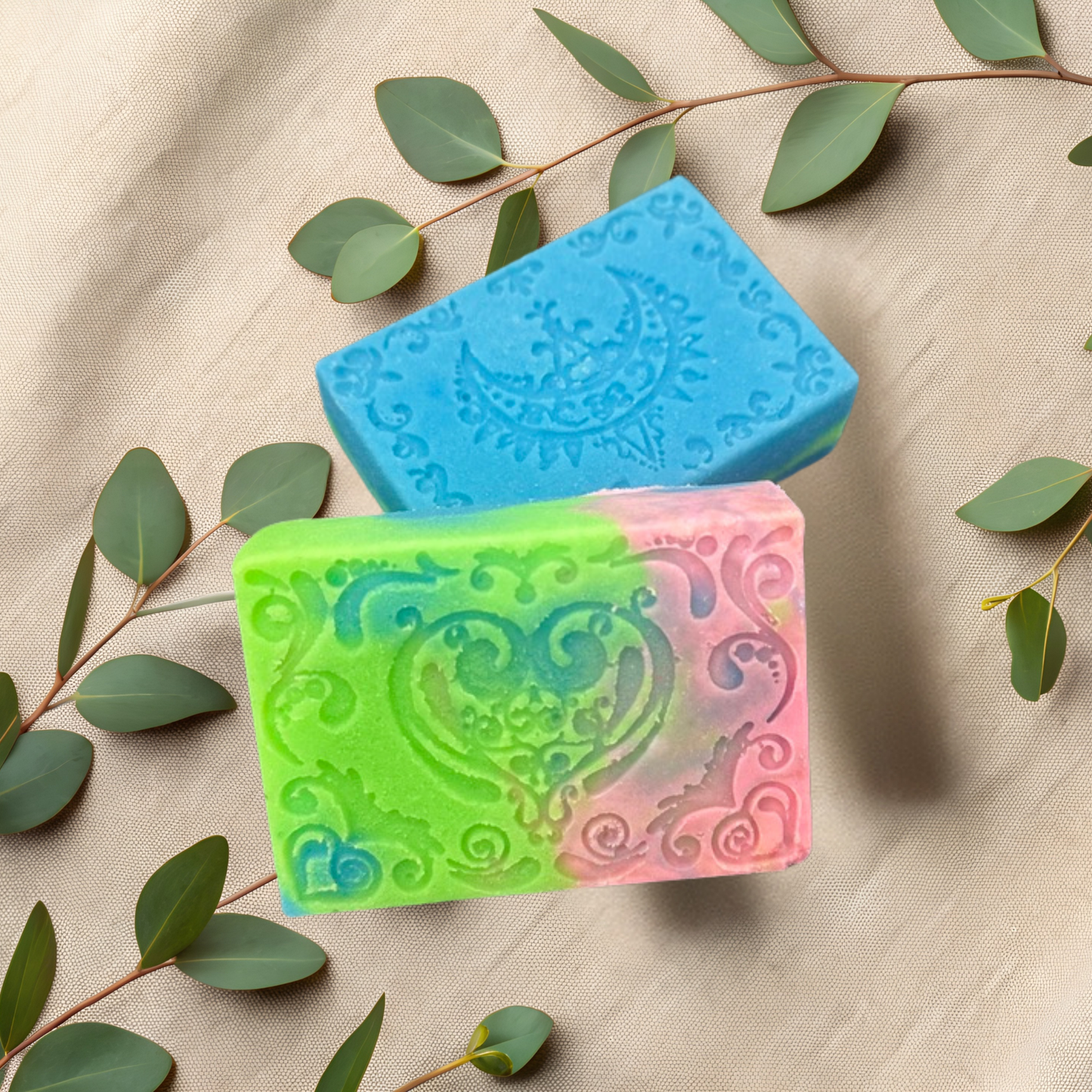 Three colorful soap bars with intricate designs on a beige fabric background with green leaves.