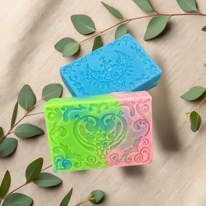 Three colorful soap bars with intricate designs on a beige fabric background with green leaves.