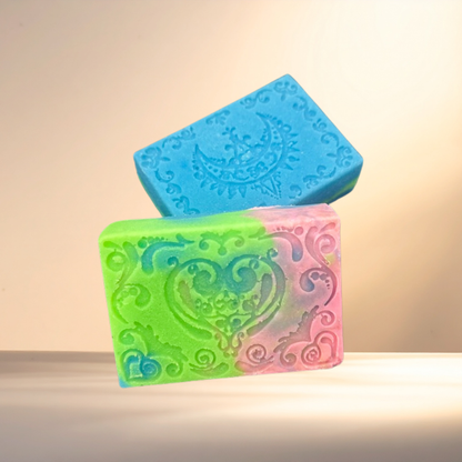 Two decorative soap bars, one blue and one pink with intricate patterns, on a light background.