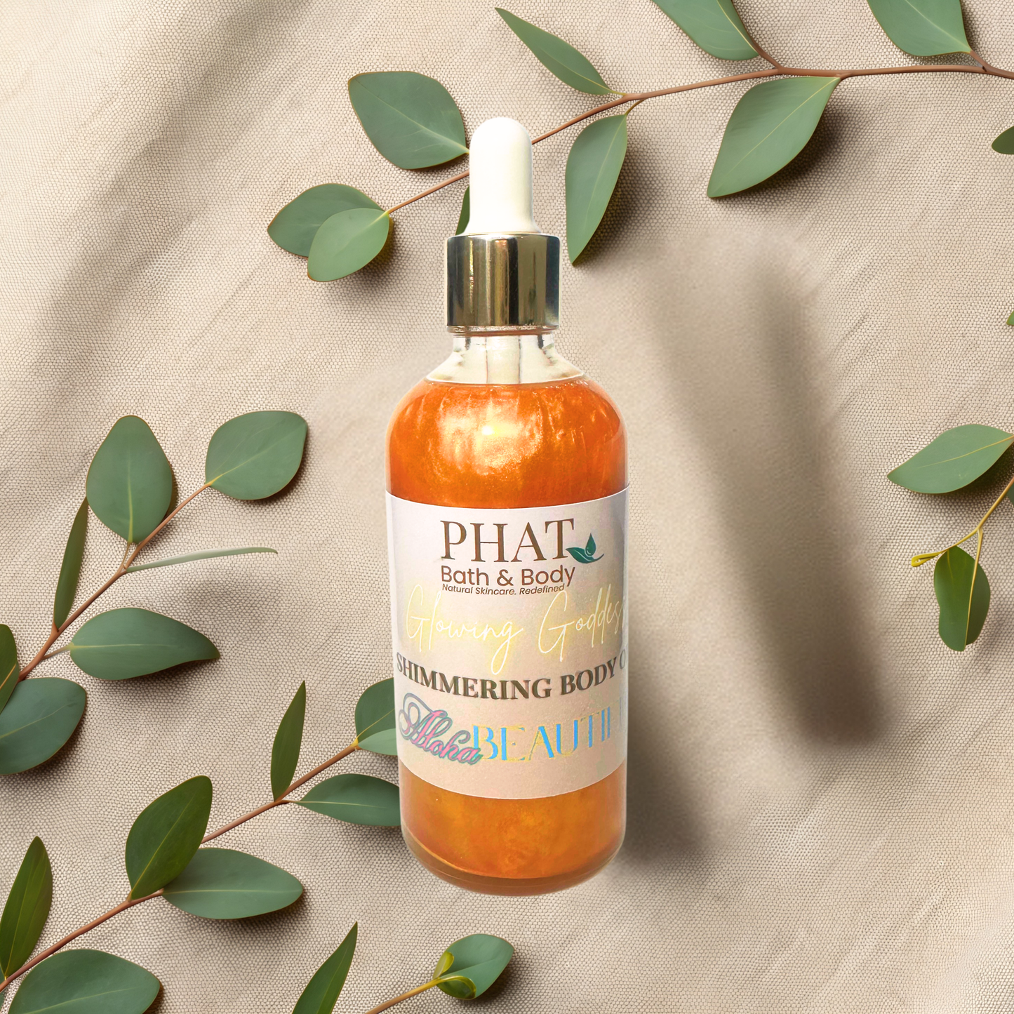 Bottle of 'PHAT Bath & Body' shimmering body oil with green leaves on a beige fabric background