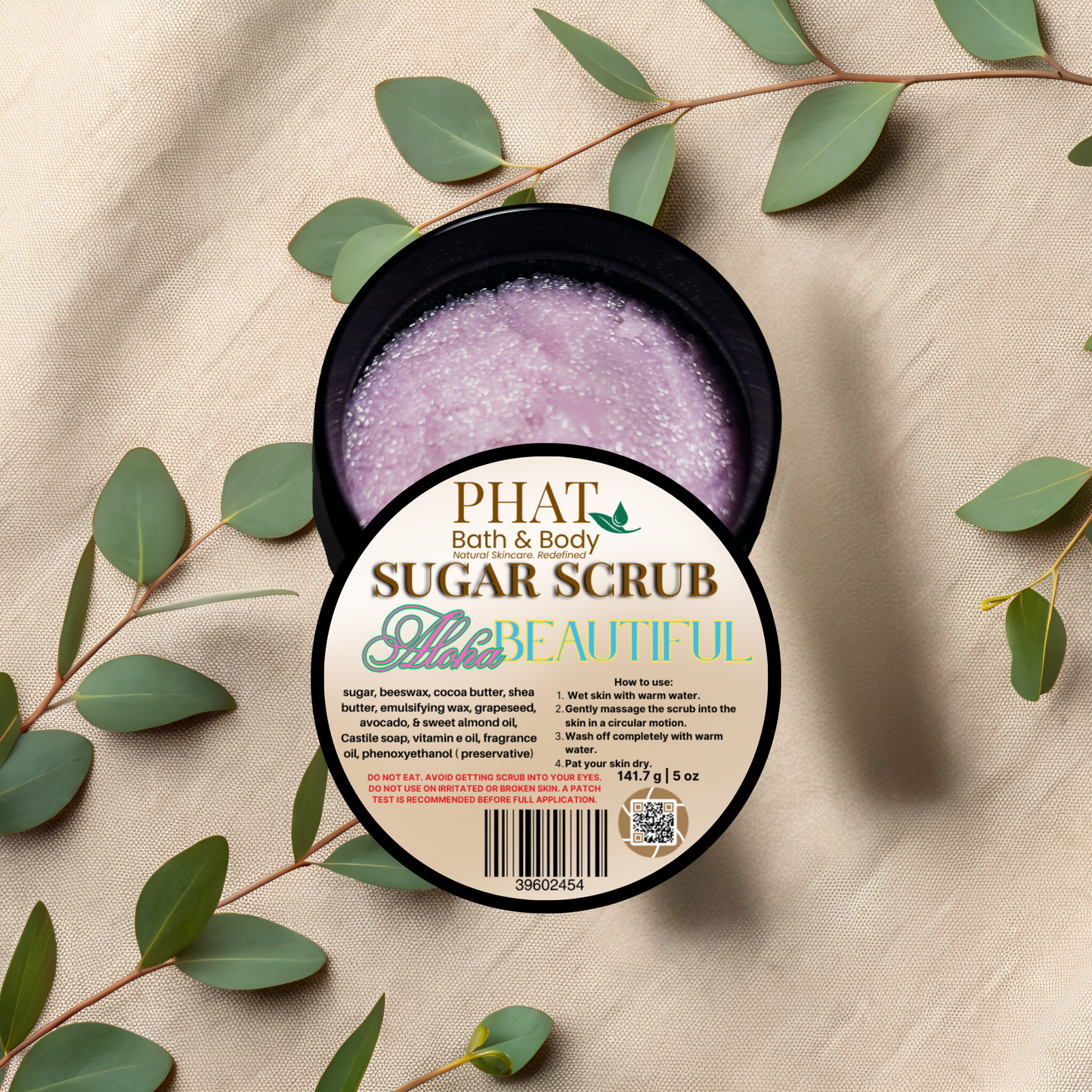 Open container of sugar scrub with a label on a beige fabric background with green leaves.