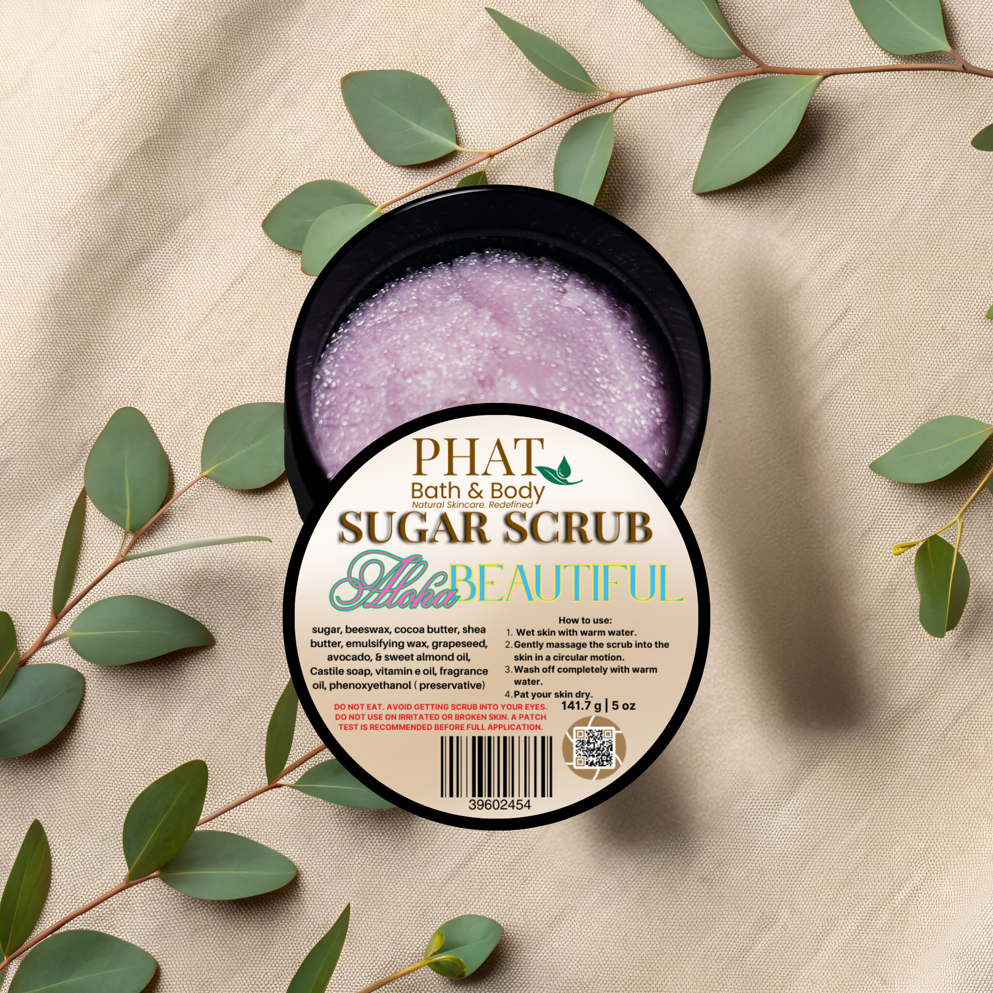 Open container of sugar scrub with a label on a beige fabric background with green leaves.