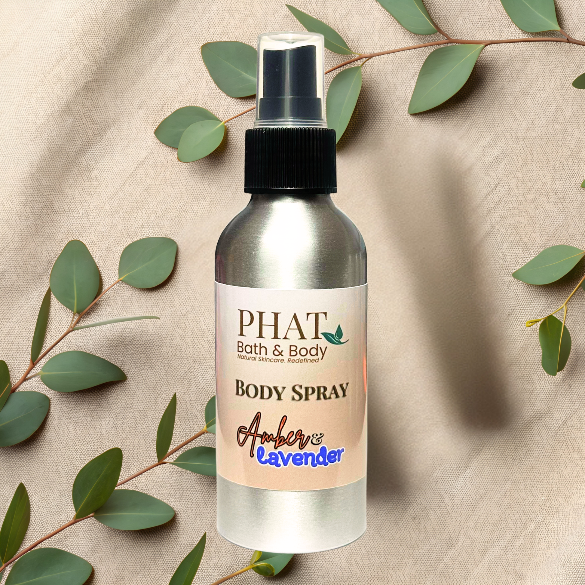 Body spray bottle with 'Phat Bath & Body' label on a beige fabric background with green leaves.