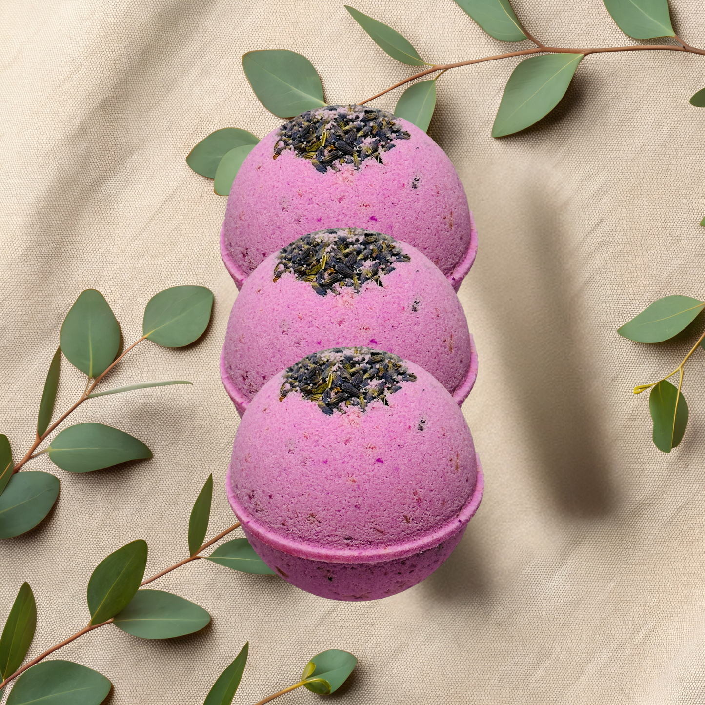 Three purple bath bombs with green leaves on a beige fabric background