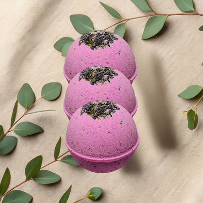 Three purple bath bombs with green leaves on a beige fabric background