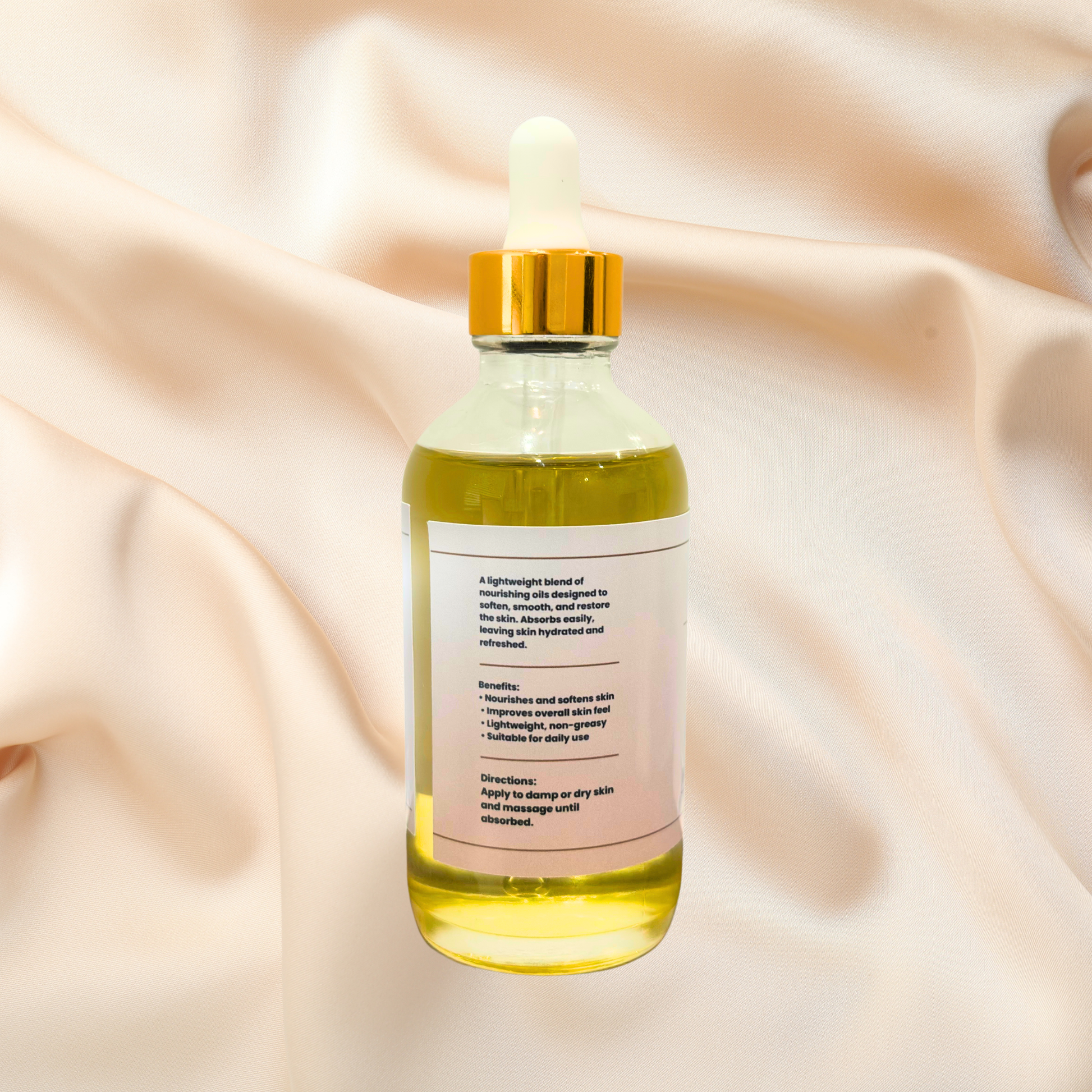 A clear glass dropper bottle filled with pale yellow oil, featuring a white label and a shiny gold cap, set against a draped satin fabric background.