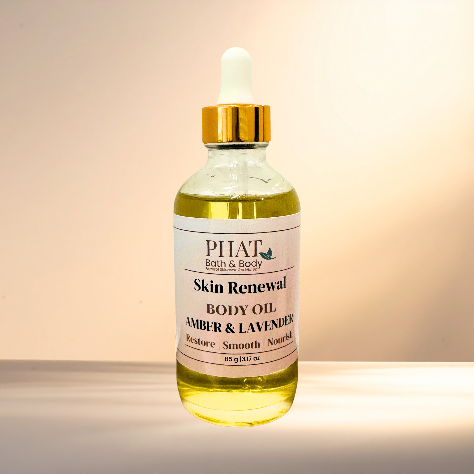 A glass bottle of PHAT Bath & Body Skin Renewal Body Oil in the Amber & Lavender scent, featuring a gold cap and white label, set against a warm beige background.