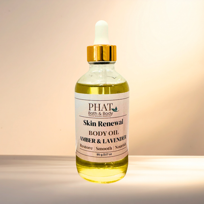 A glass bottle of PHAT Bath & Body Skin Renewal Body Oil in the Amber & Lavender scent, featuring a gold cap and white label, set against a warm beige background.