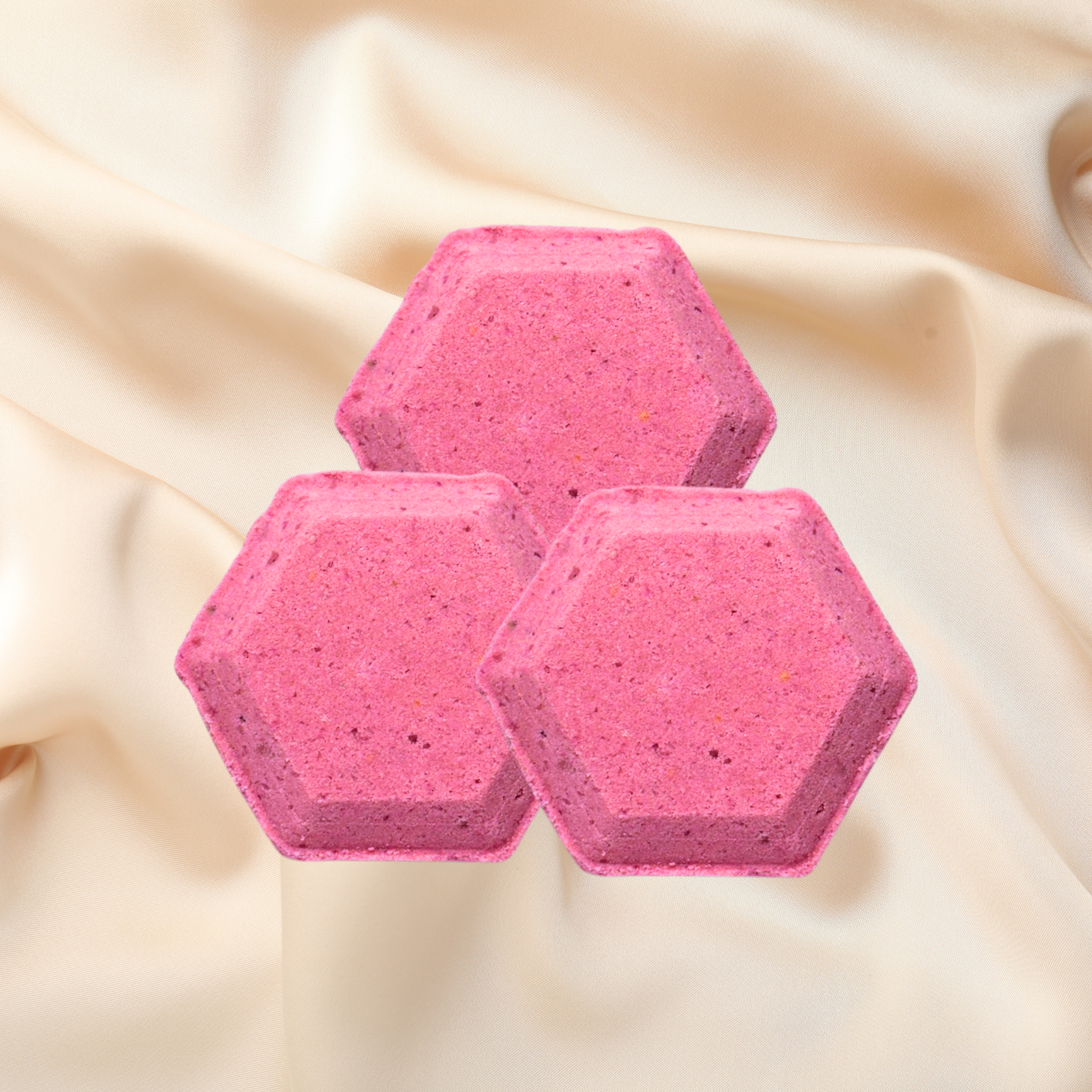 Three pink hexagonal shower bombs on a beige fabric background