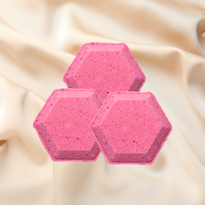 Three pink hexagonal shower bombs on a beige fabric background