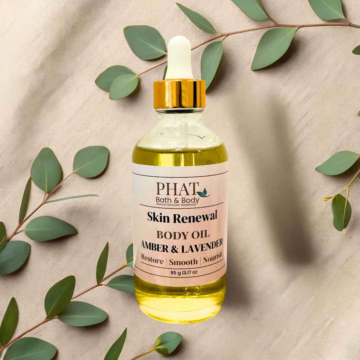 A bottle of PHAT Bath & Body Skin Renewal Body Oil (Amber & Lavender) with a gold dropper cap, styled on a beige fabric background with eucalyptus leaves.