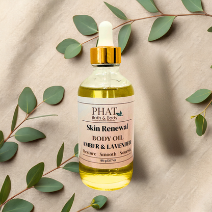 A bottle of PHAT Bath & Body Skin Renewal Body Oil (Amber & Lavender) with a gold dropper cap, styled on a beige fabric background with eucalyptus leaves.