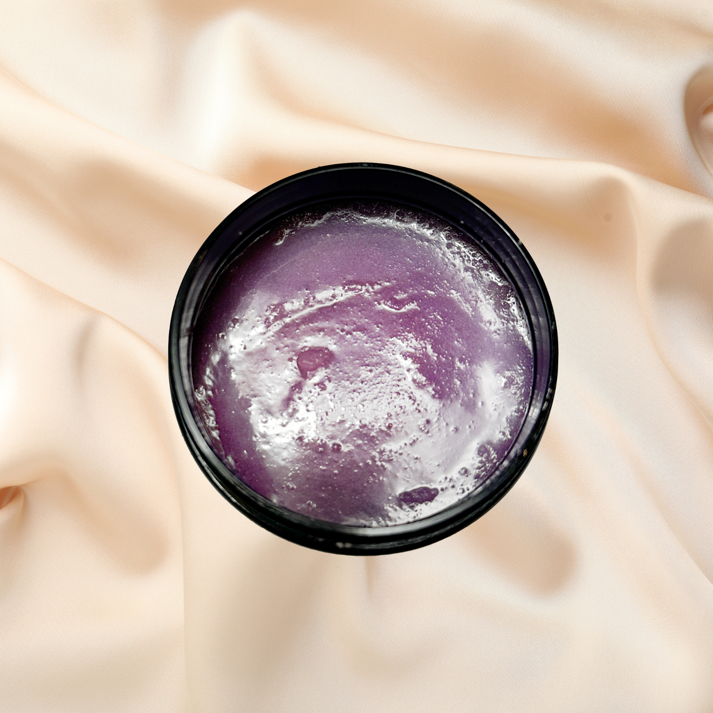 Purple scrub in a black container on beige fabric