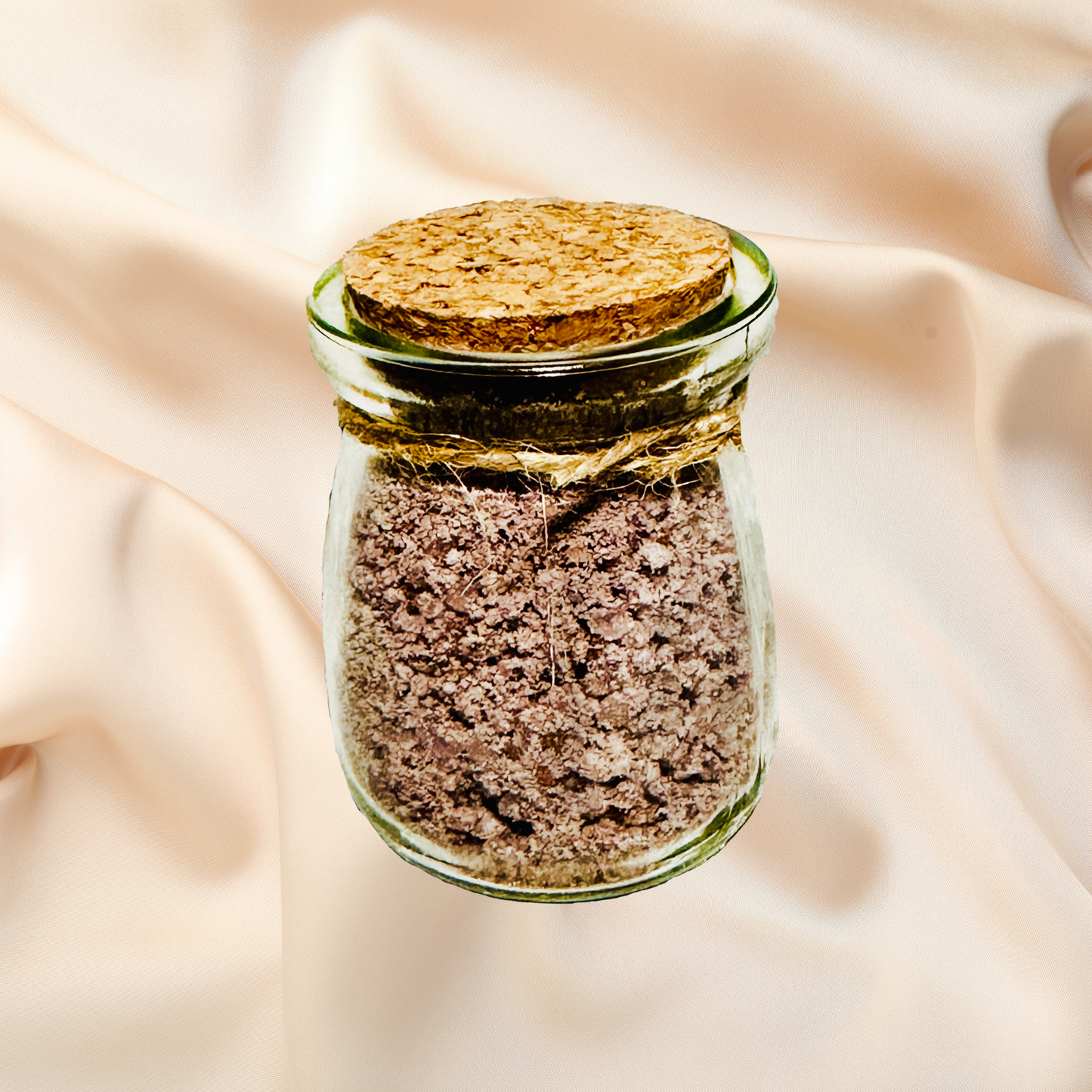 Glass jar with cork lid containing a brown bath salts on a beige fabric background