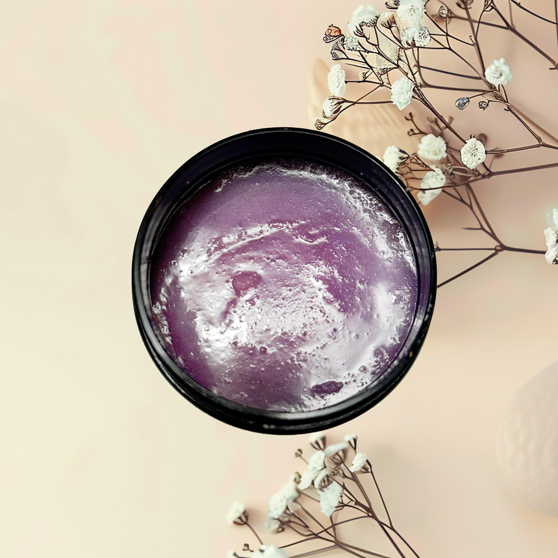 Purple scrub in a black container with white flowers on a beige background