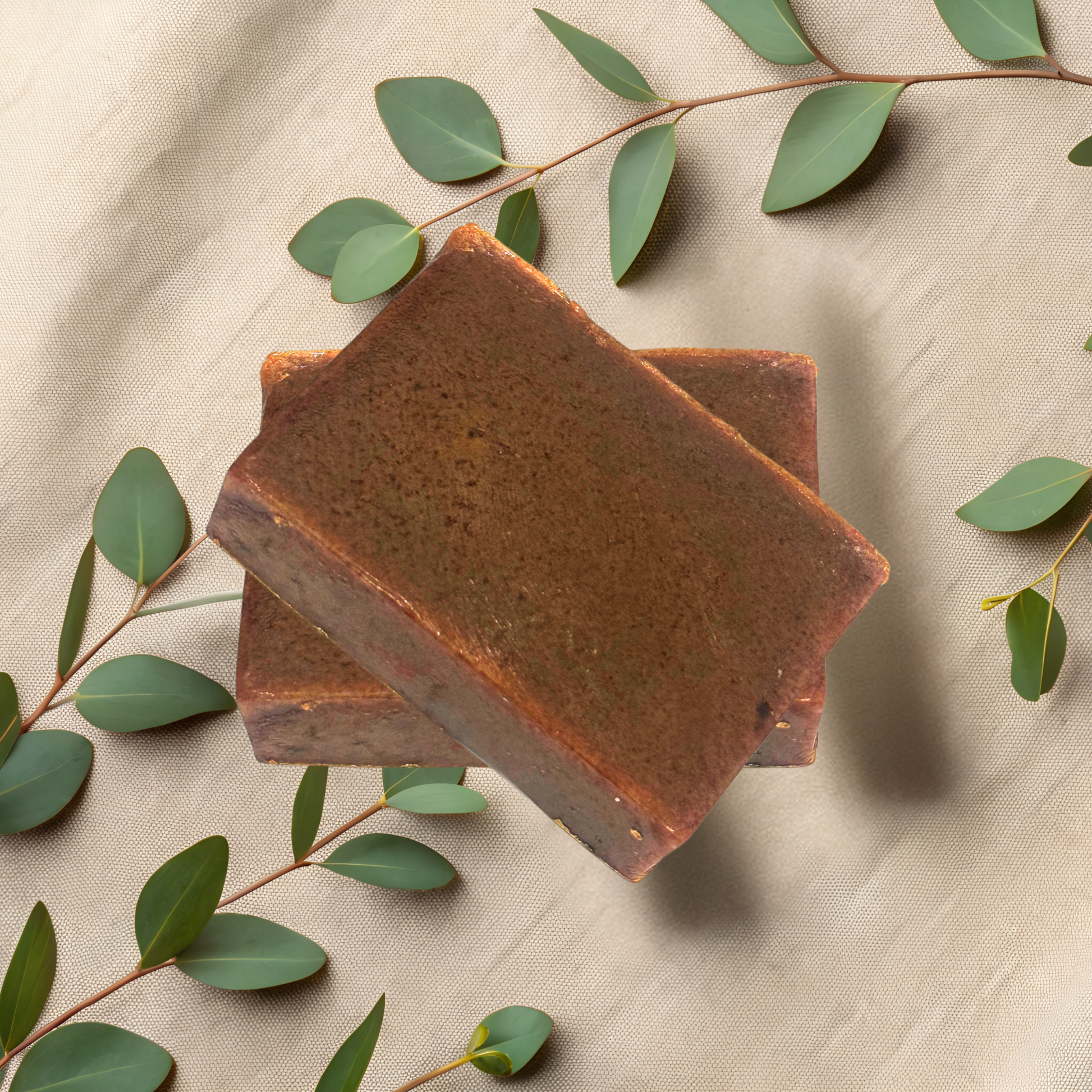 Two brown soap bars on a beige fabric background with green leaves.