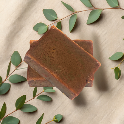 Two brown soap bars on a beige fabric background with green leaves.