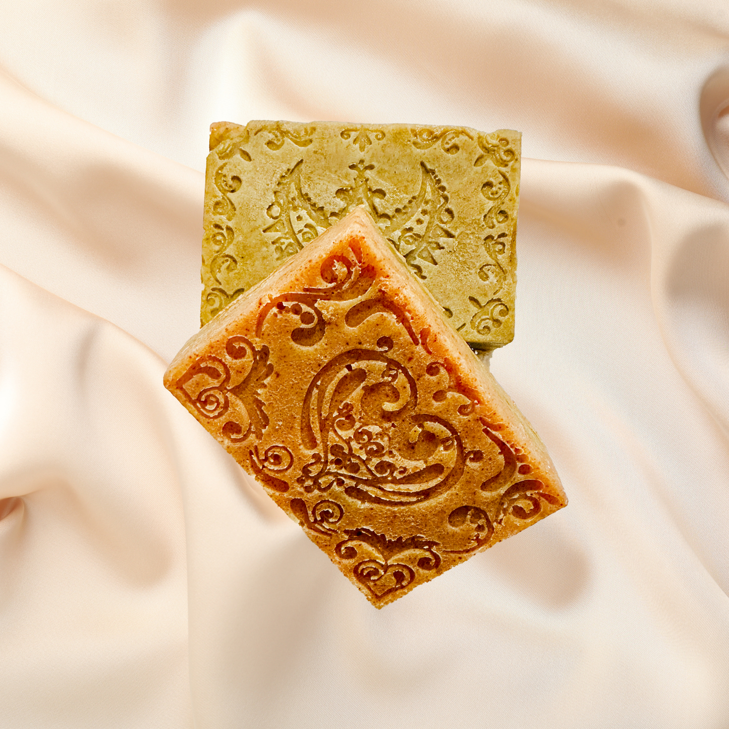 Two soap bars with decorative patterns on a soft fabric background