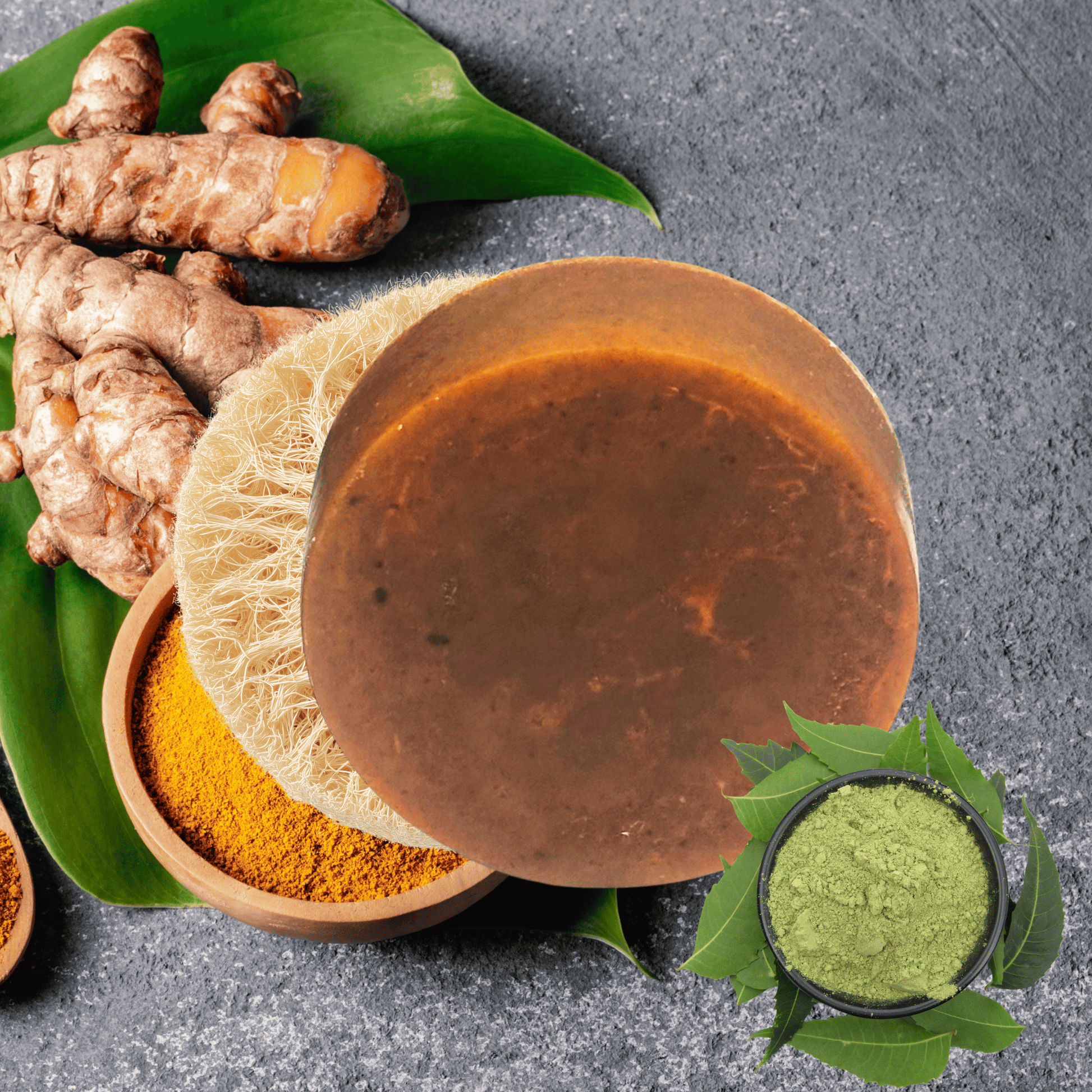 Brown soap with turmeric powder, fresh turmeric roots, and green leaves on a gray surface