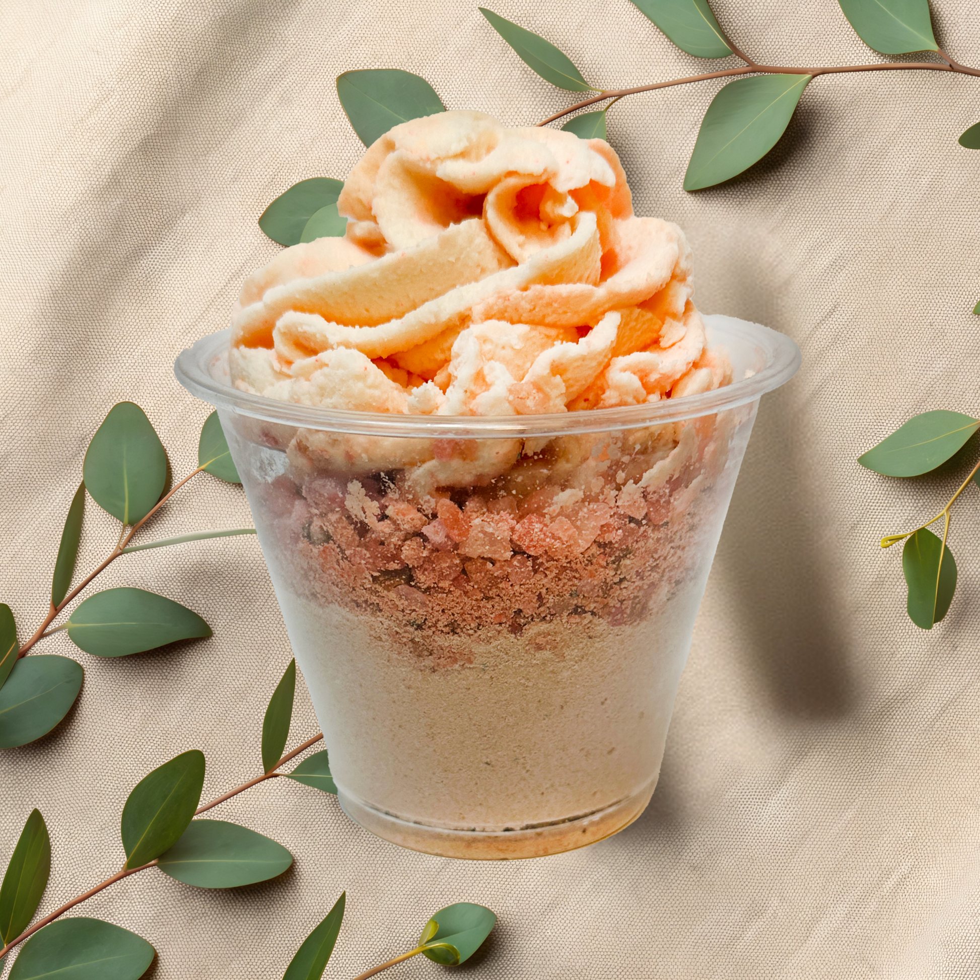 Bath parfait in a clear cup with green leaves on a beige fabric background