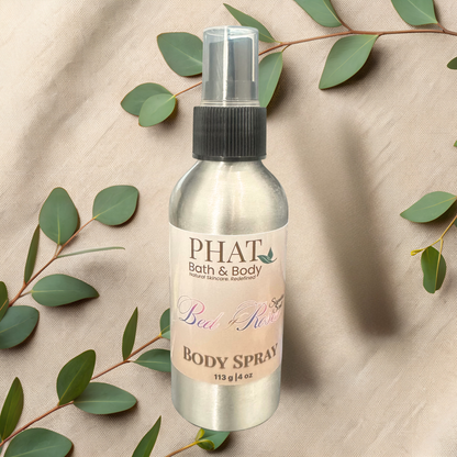 Body spray bottle with 'PHAT Bath & Body' label on a beige fabric background with green leaves.