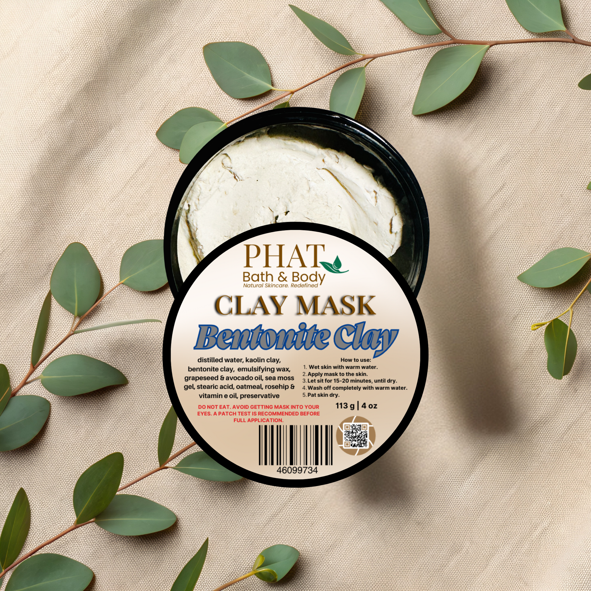 Clay mask container with 'Phat Bath & Body' label on a beige fabric background with green leaves.