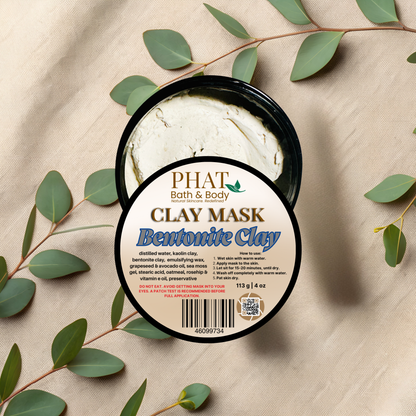 Clay mask container with 'Phat Bath & Body' label on a beige fabric background with green leaves.