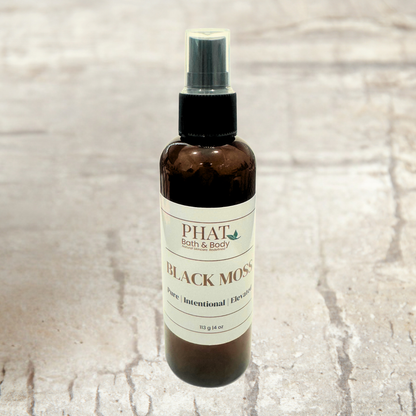 Brown spray bottle labeled 'PHAT Bath & Body Black Moss' on a textured beige background