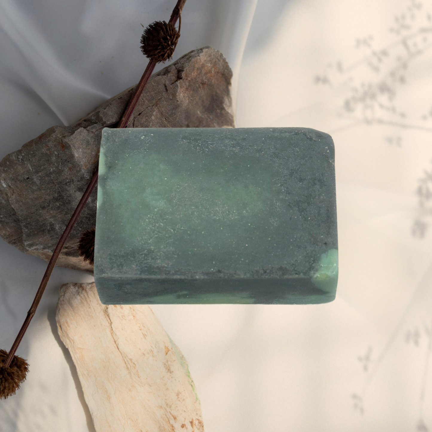 Green bar of soap on a white background with rocks and twigs