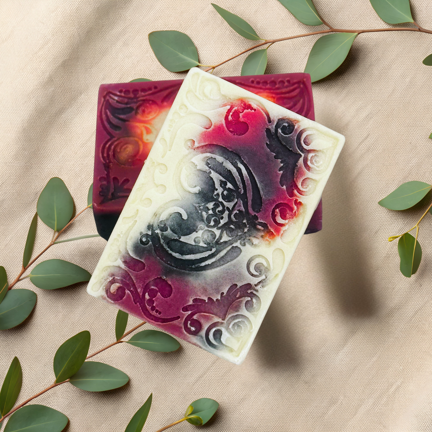 Decorative soap bars with intricate designs on a beige fabric background with green leaves.