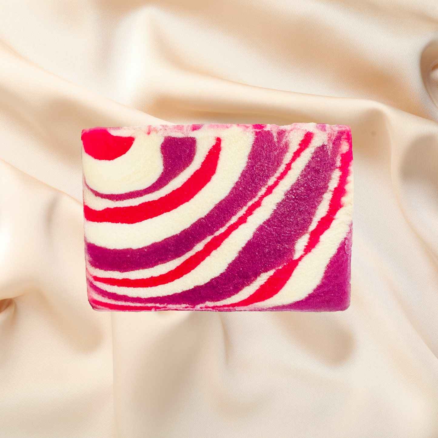Bar of soap with pink and red swirl pattern on a beige fabric background
