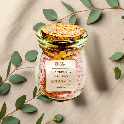 Jar of blackberry vanilla bath salts with a cork lid on a beige fabric background with eucalyptus leaves.