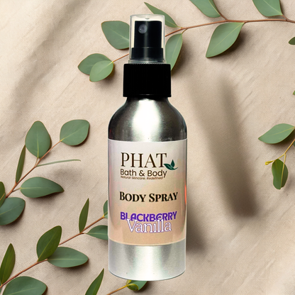 Body spray bottle labeled 'PHAT Bath & Body' with 'Blackberry Vanilla' scent on a beige fabric background with green leaves.