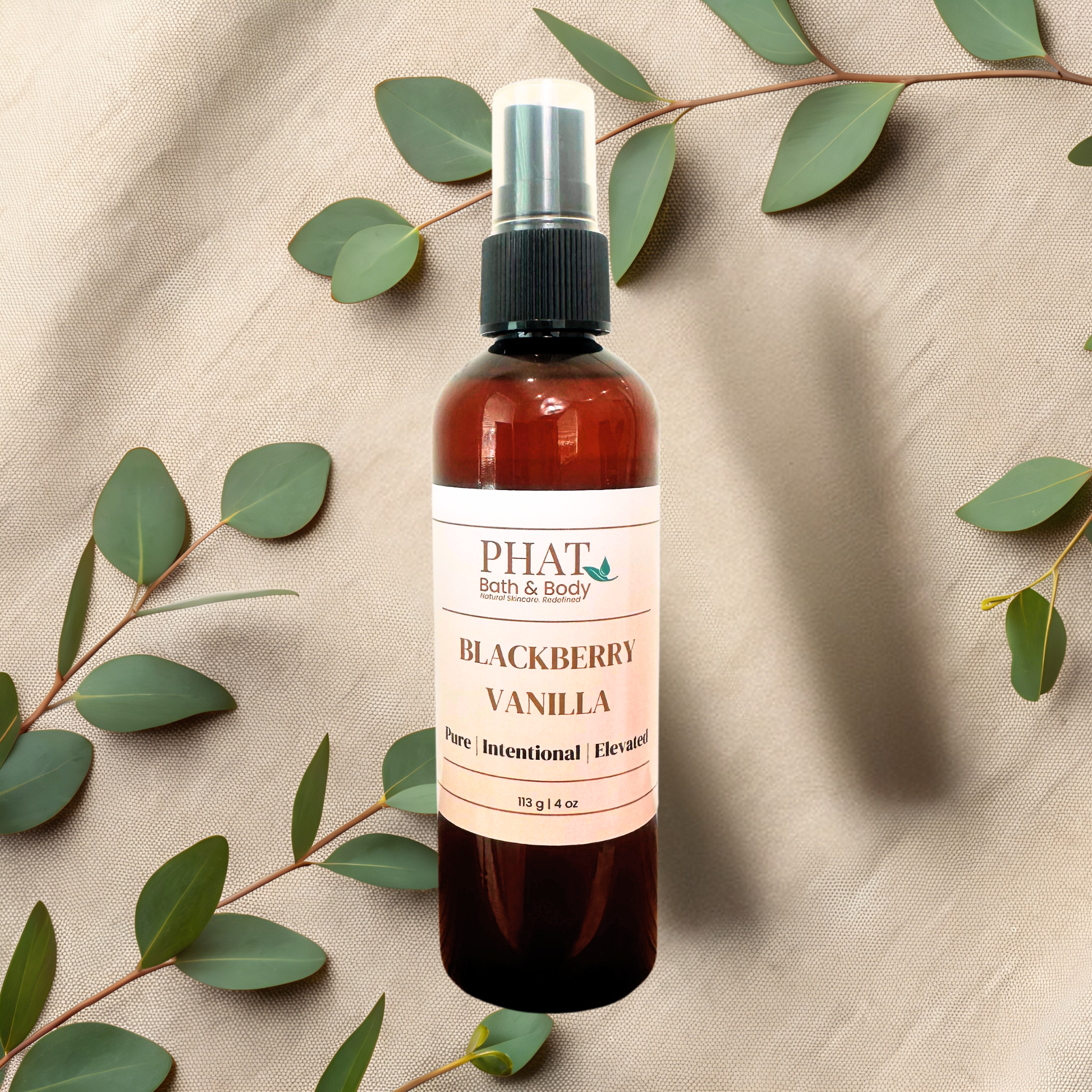 An amber spray bottle labeled PHAT Bath & Body Blackberry Vanilla, styled on a beige fabric background with eucalyptus leaves.
